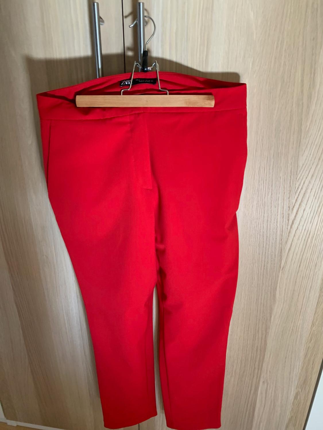 Red trousers hanging on a wooden hanger over a light wooden door. The ZARA label is visible.