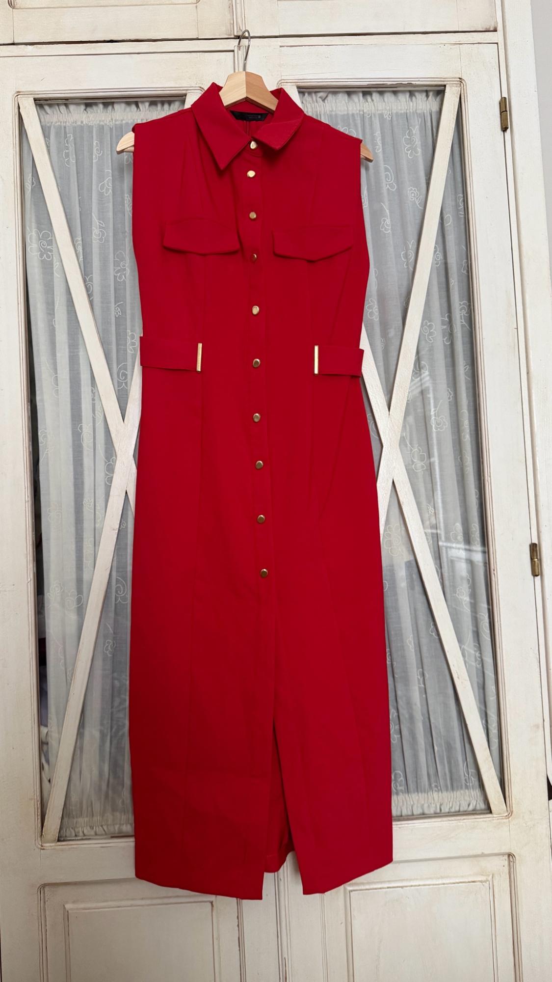 Sleeveless red shirt dress with gold buttons, hanging on a wooden hanger in front of a white door with curtains.