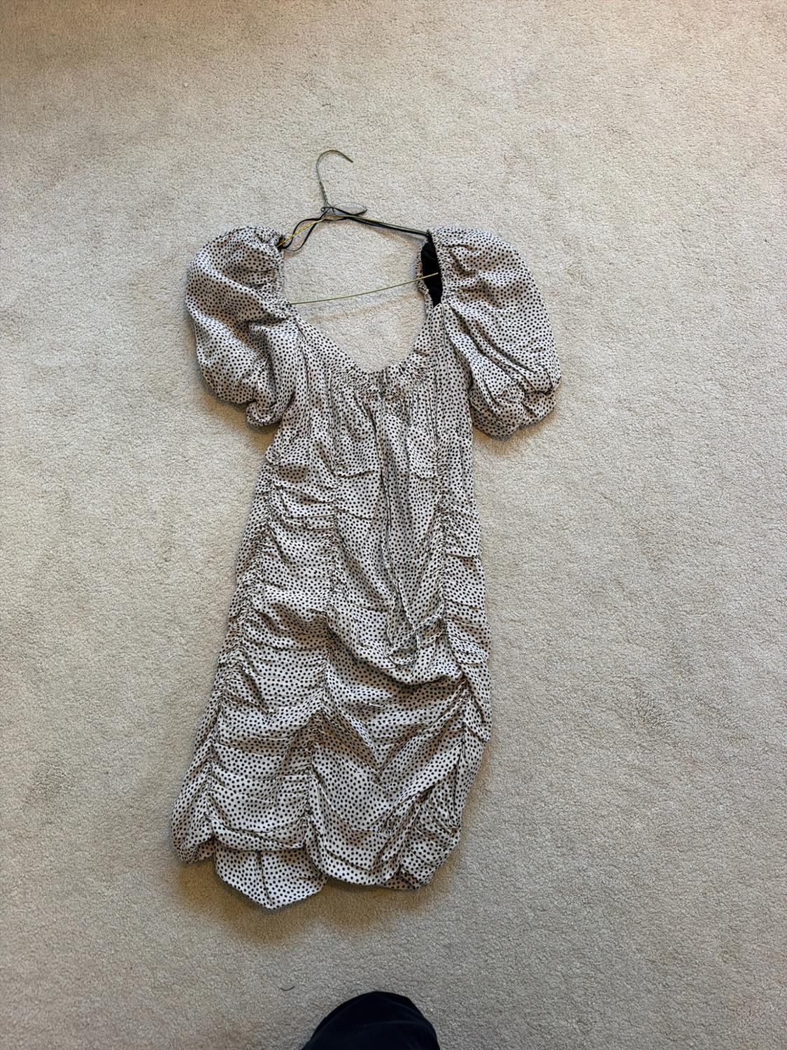 Light-coloured short dress with black polka dots, puff sleeves and ruched design, on a hanger against a beige carpeted floor.