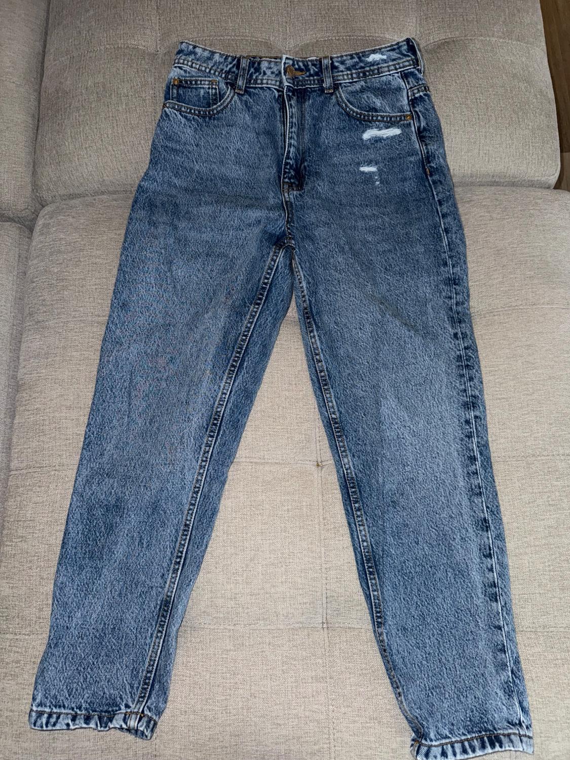 Distressed blue jeans on a beige couch, featuring ripped details on the right leg and five visible pockets.