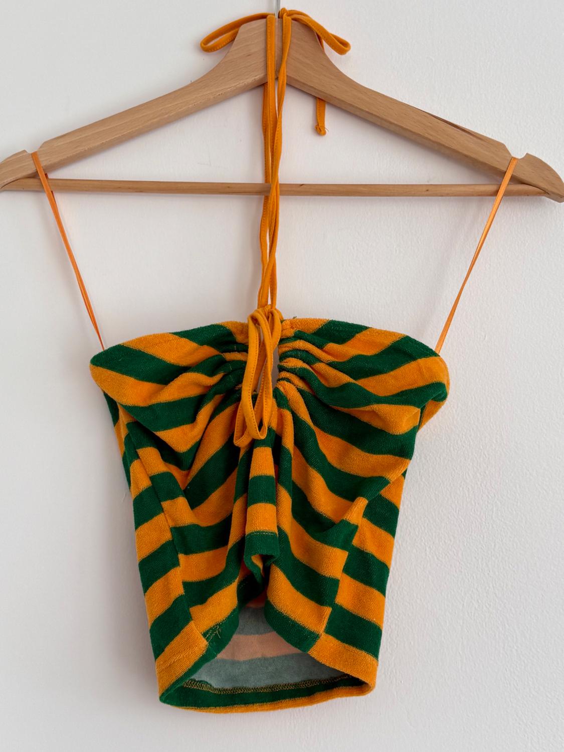 Strappy top with green and orange horizontal stripes, hanging on a wooden hanger against a white wall.