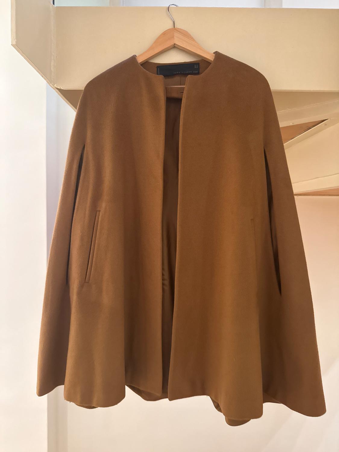Brown coat hanging on a wooden hanger, with a minimalist design and no visible buttons, in a lit indoor setting.