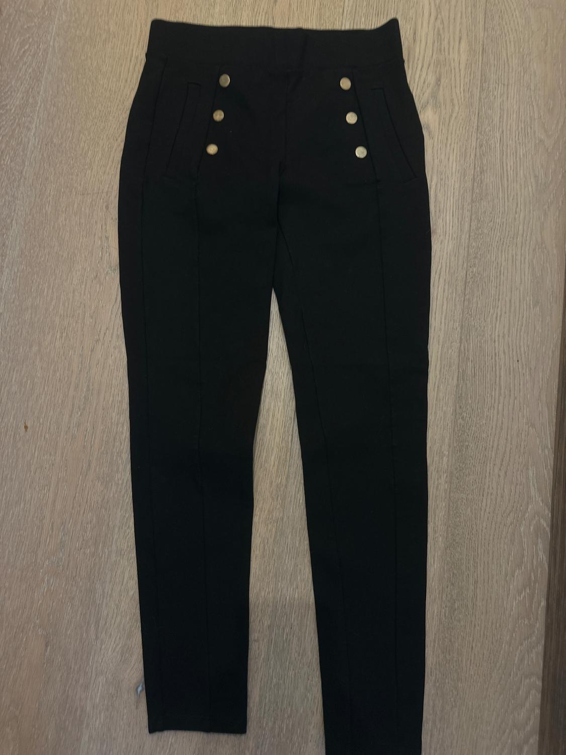Black trousers with gold buttons on the front, placed on a light wooden floor.