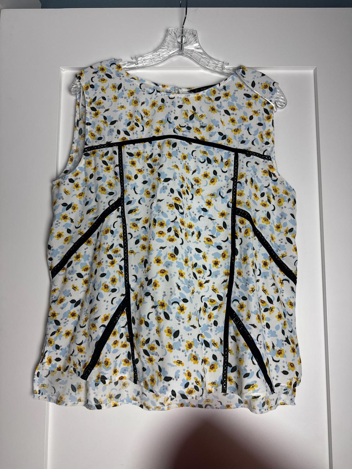 Yellow and blue floral print sleeveless blouse with black lace details, hanging on a hanger over a white door.