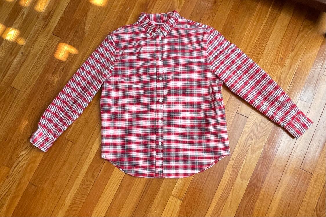 Long-sleeve button-up shirt with a red-and-white plaid print, laid out on a wooden floor.