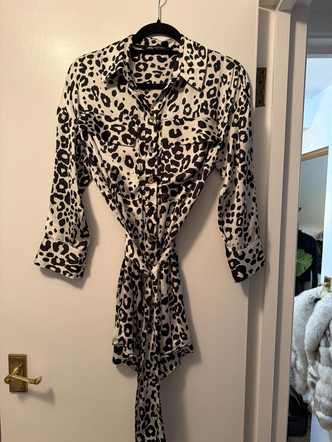 Black and white leopard print long-sleeved shirt hanging on a black hanger over a white door.