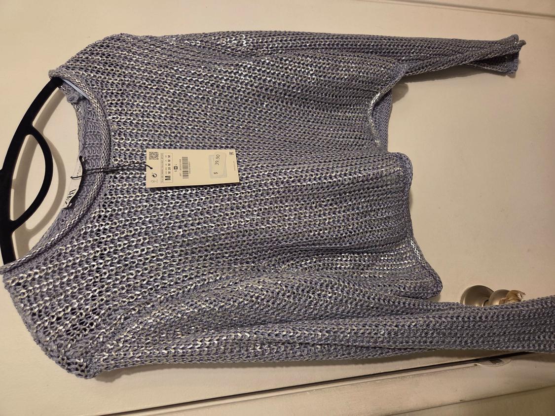 Light blue metallic knit sweater folded on a white surface. Displays tags with the text ZARA, M and $ 39.90.