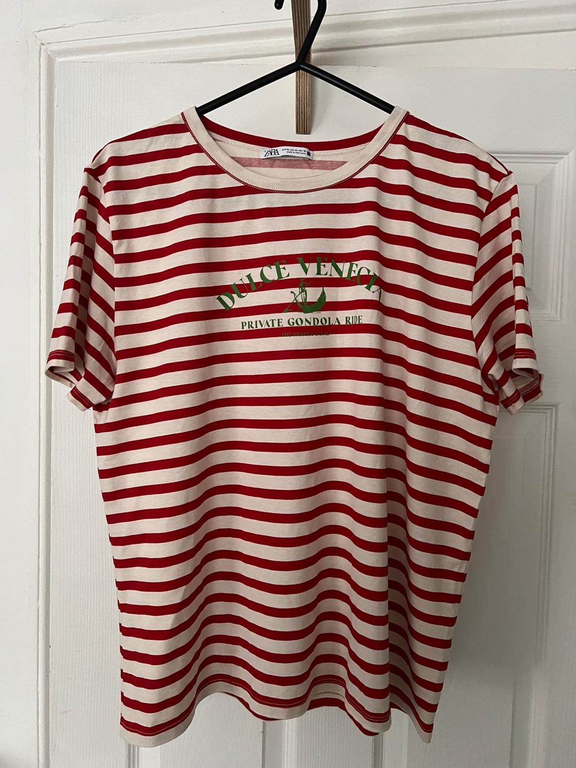 Red and white striped t-shirt hanging on a hanger. Text on the front: "SWEET VENICE PRIVATE GONDOLA RIDE".