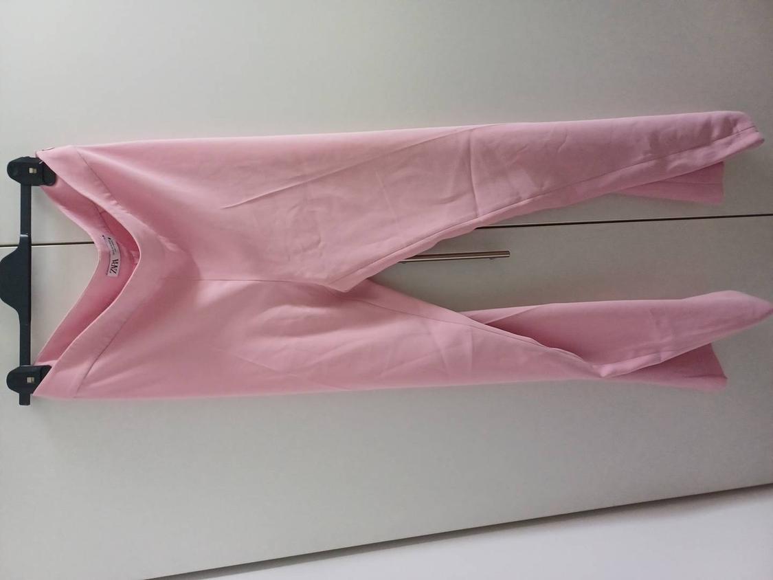 Pink trousers hanging on a black hanger in front of a white background. Label visible on the waistband.