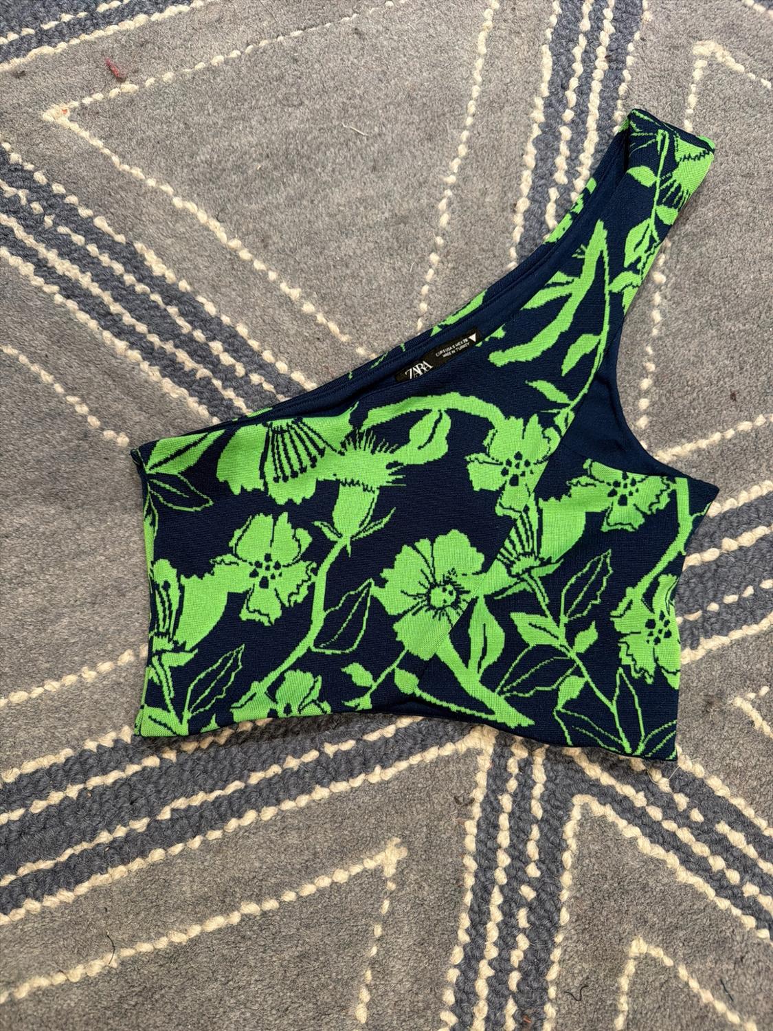 Navy blue asymmetric top with a green floral print on a grey carpet with a white pattern. Label bearing the text ZARA.