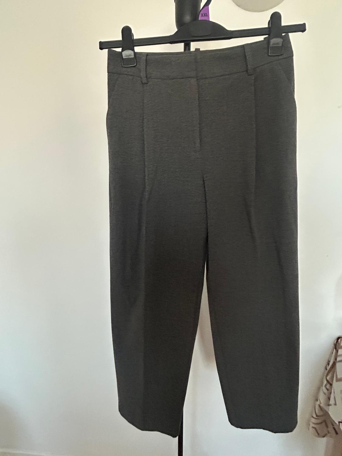Grey trousers hanging on a black hanger with clips. White background and purple tag with "XXL" visible at the top.