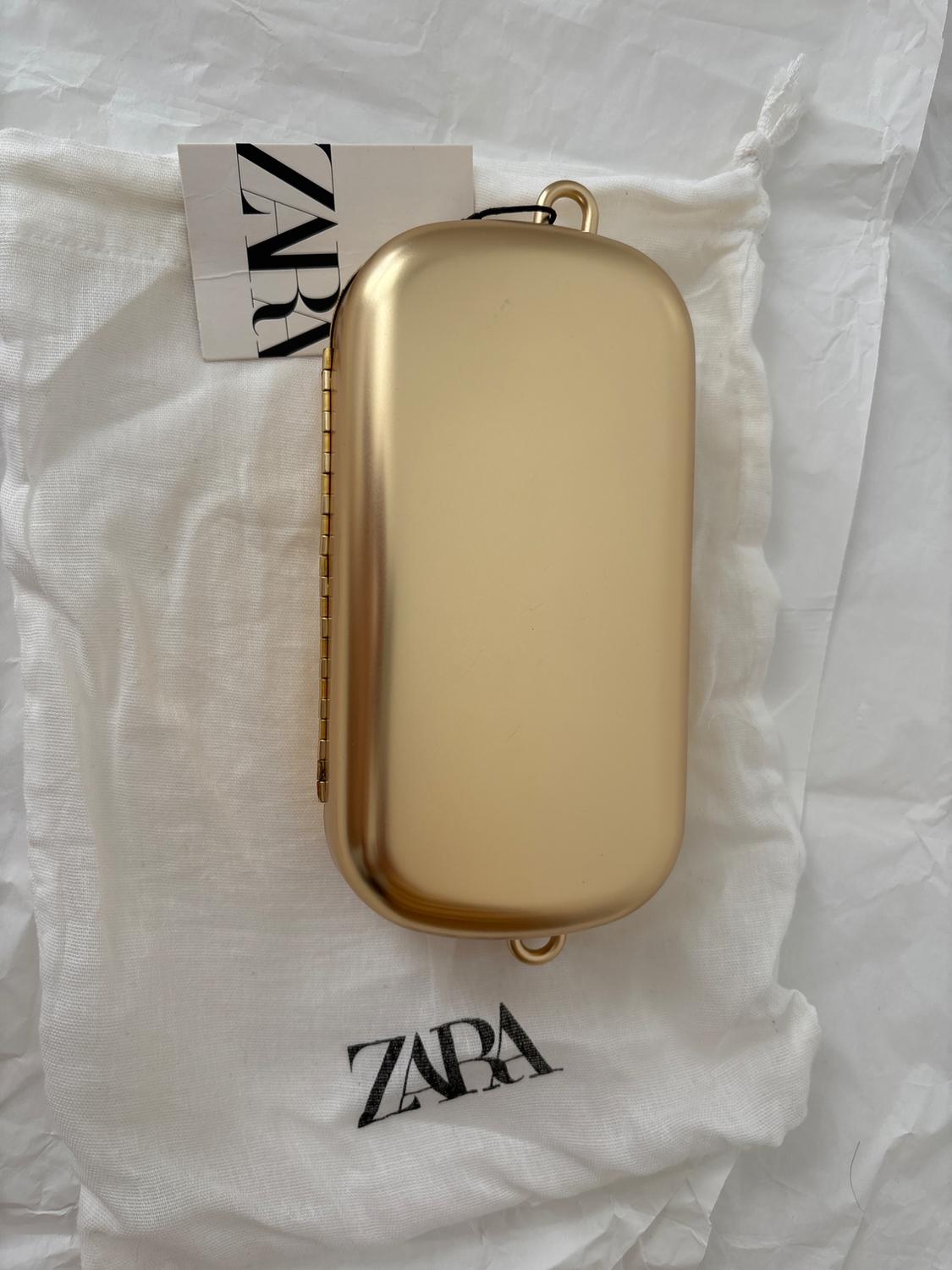 Golden case on a white bag with the "ZARA" logo in black. ZARA label visible at the top.