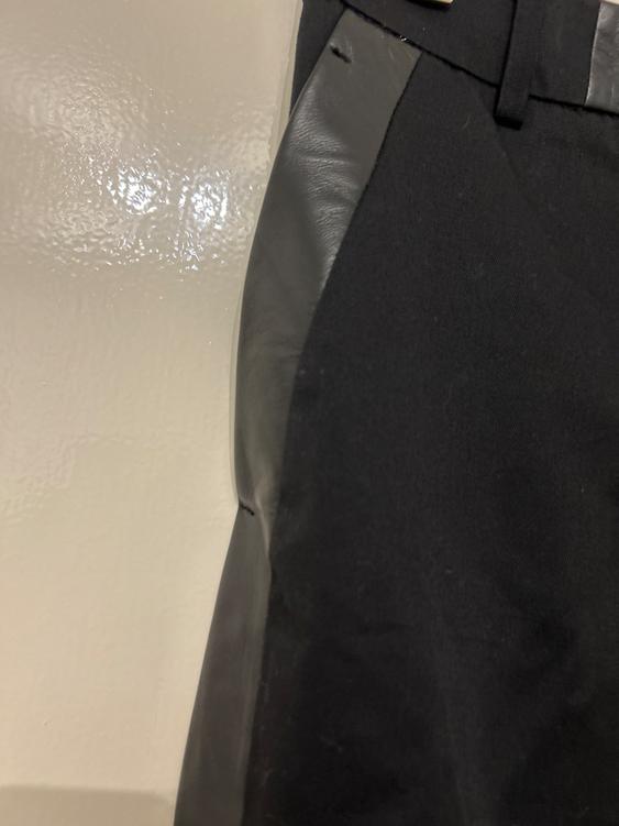 Detail of a black garment with panels of shiny material on a light background. The texture of the material is visible.