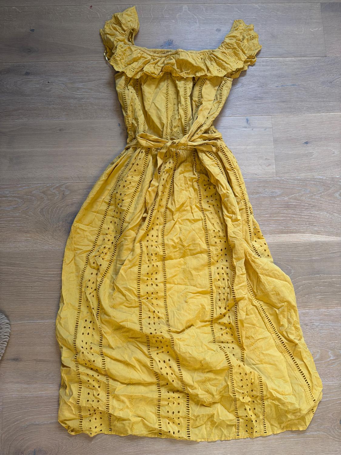 Yellow cotton dress with ruffles on the neckline and a matching belt, on a light wooden floor.