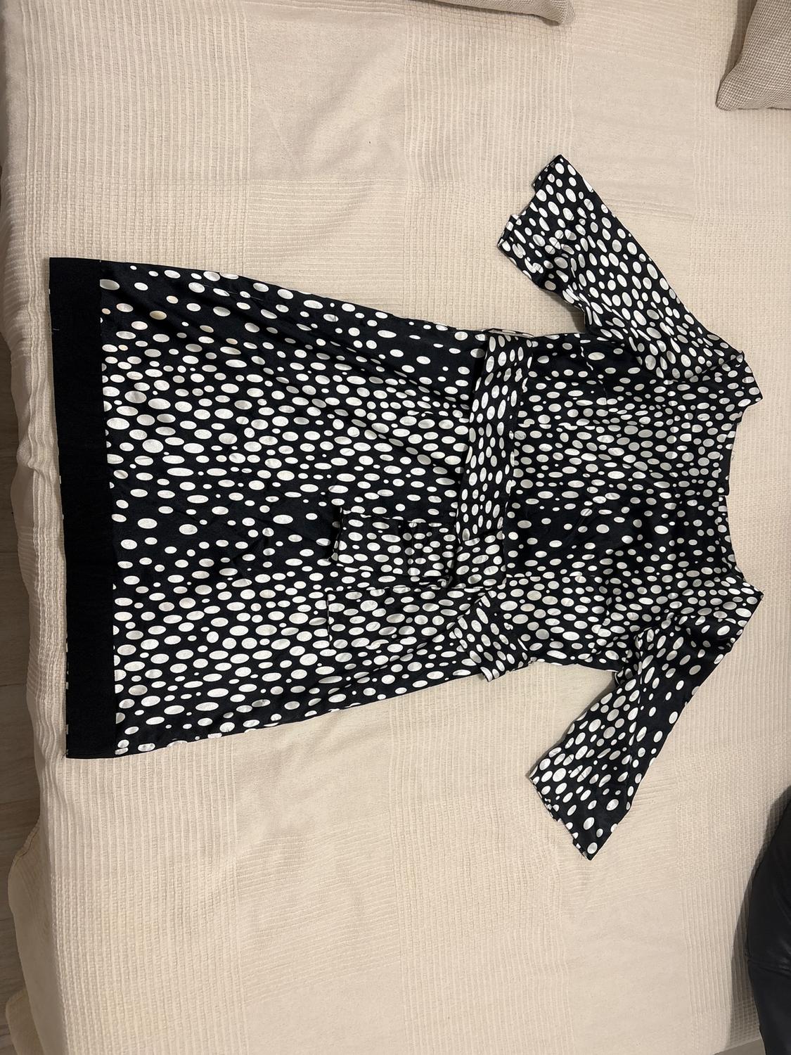 Black dress with white polka dot print, three-quarter length sleeves, laid out on a beige bed.