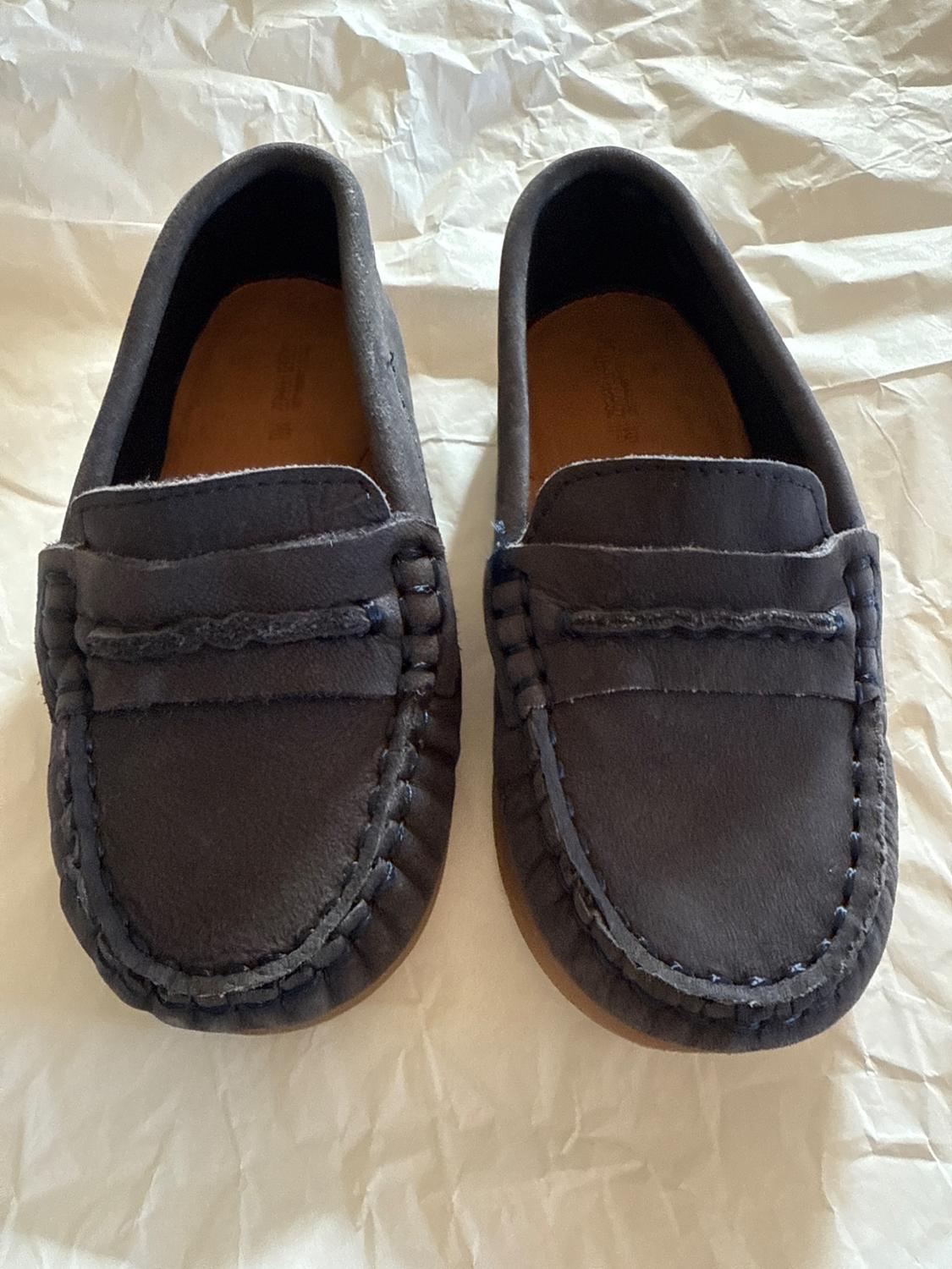 Black leather loafers with visible stitching, placed on white crumpled paper.