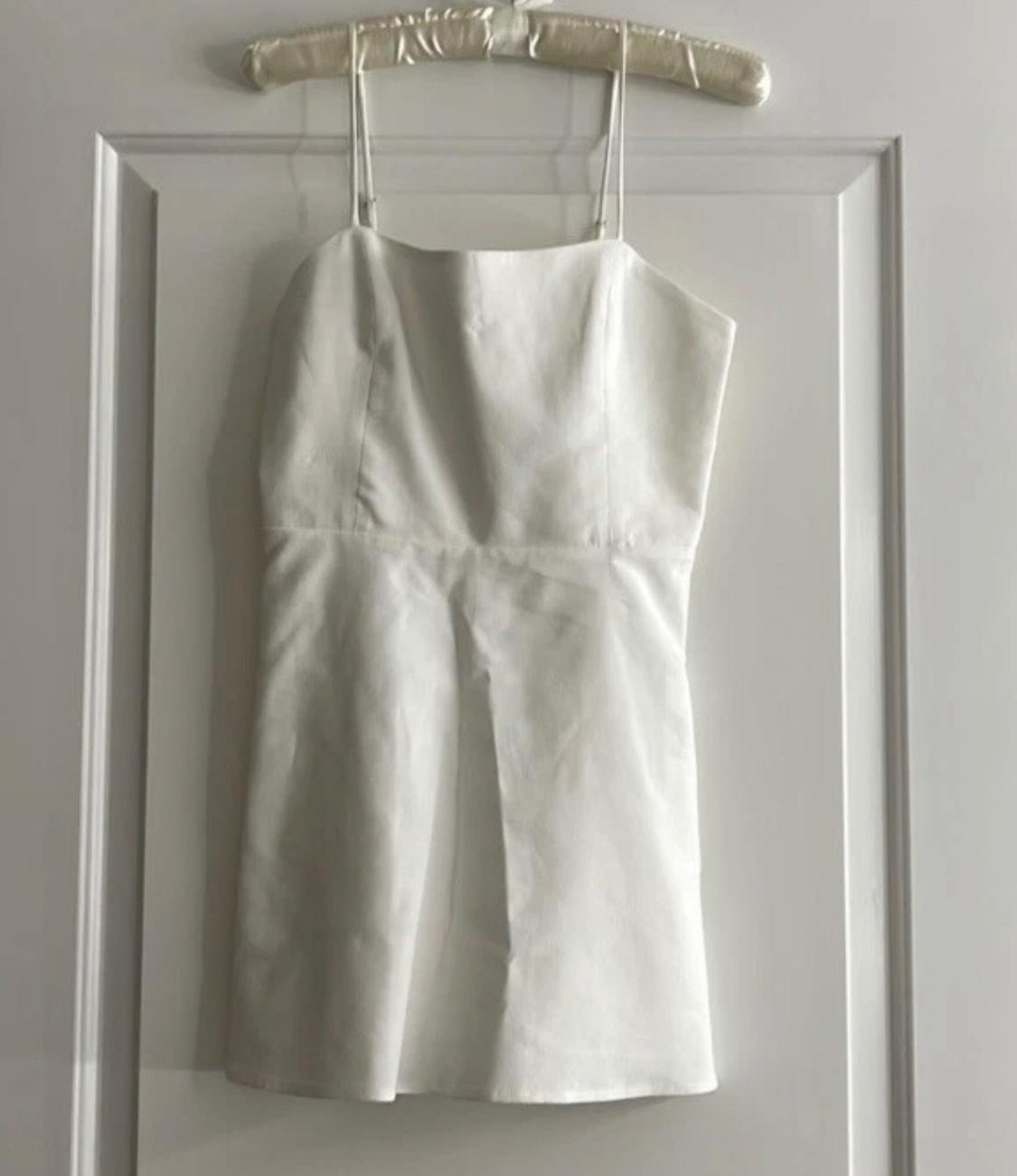 White sleeveless dress hanging on a padded hanger over a white door.