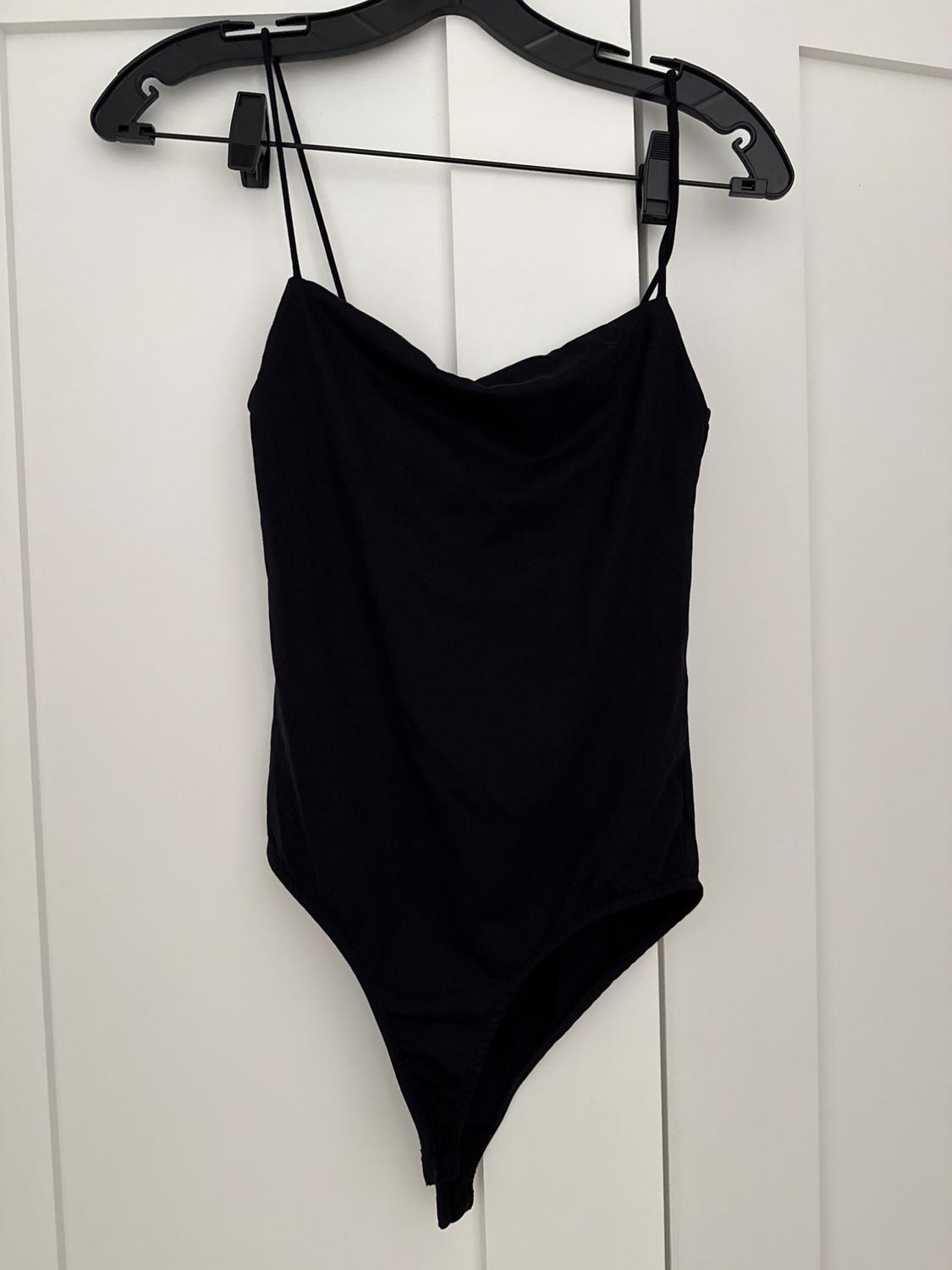 Black spaghetti strap bodysuit hanging on a black hanger over a white door.