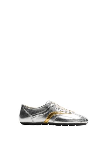 Side view of silver trainers with gold detailing, flat sole and lace-up fastening. Round toe finish.