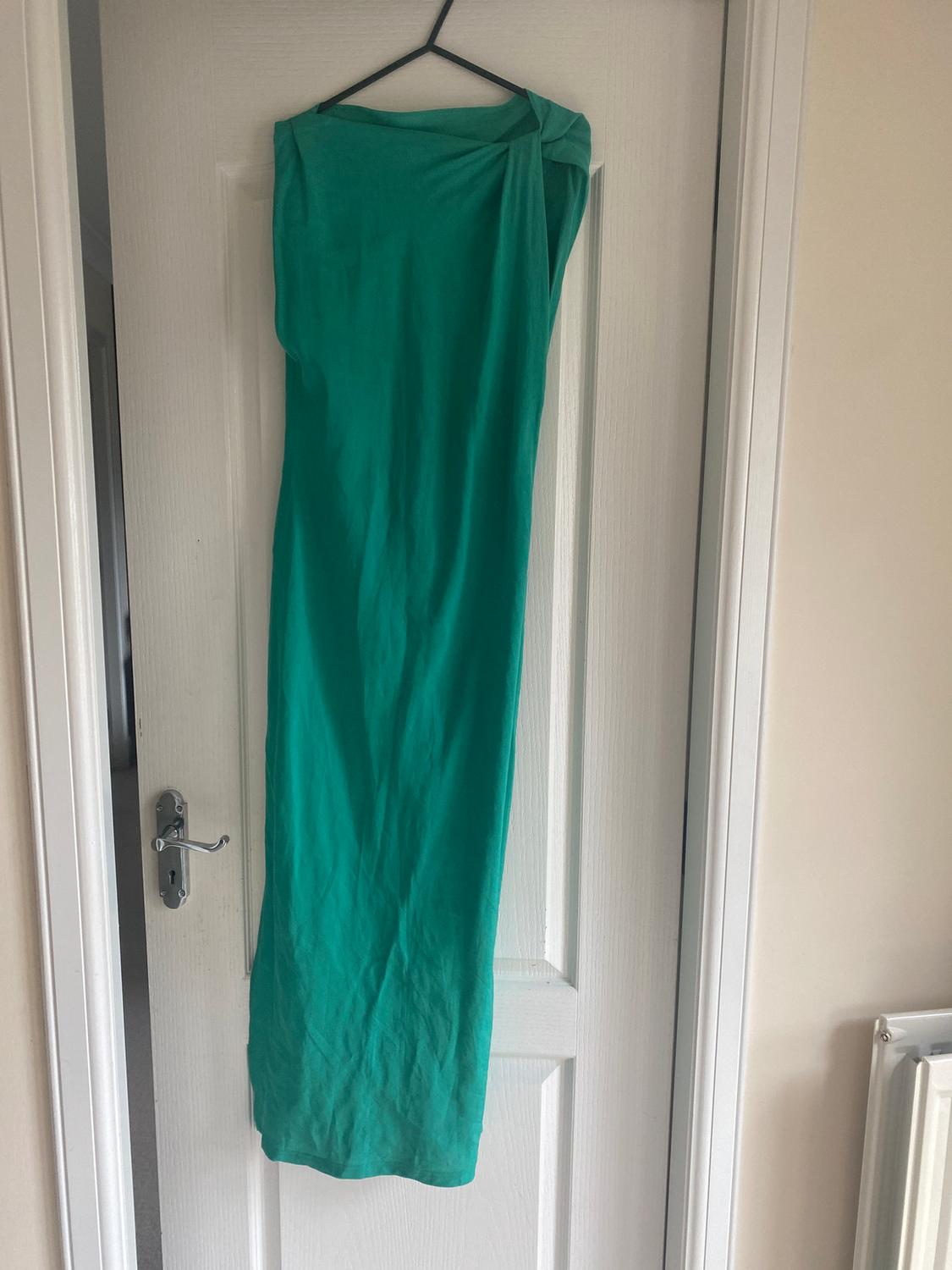 Long green dress hanging on a hanger over a white door. The fabric has a draped design on the shoulder.