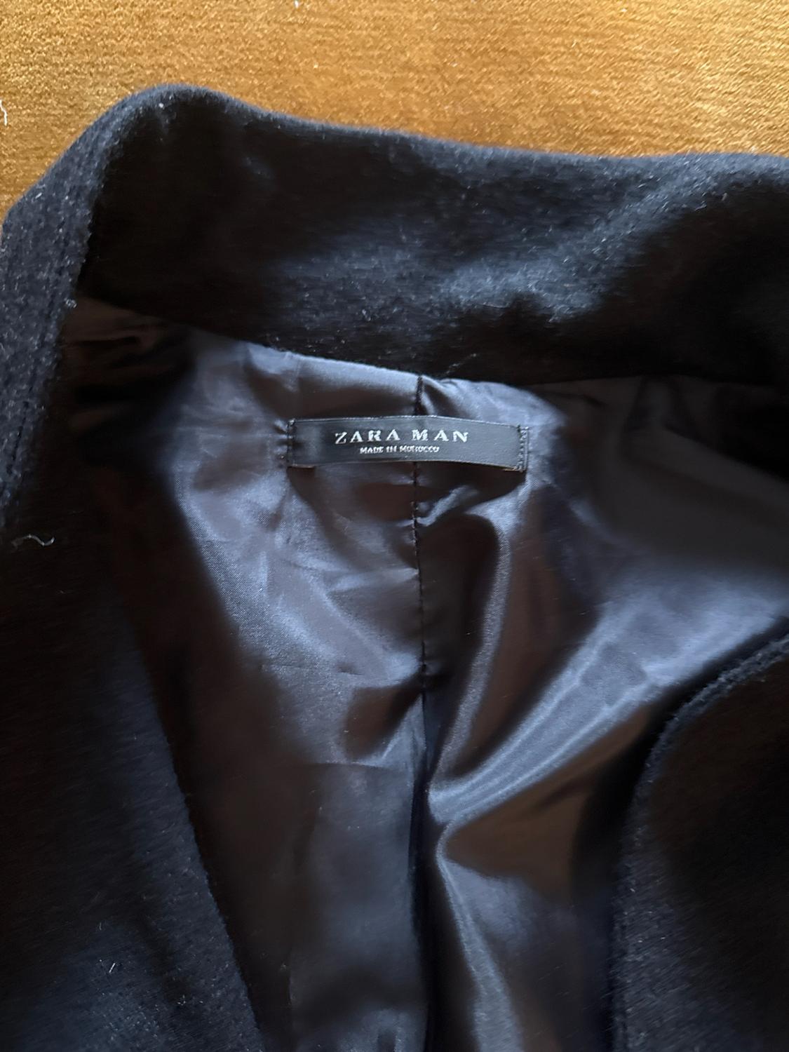 Detail of the inside of a black jacket on a mustard background. The label reads "ZARA MAN MADE IN MOROCCO".