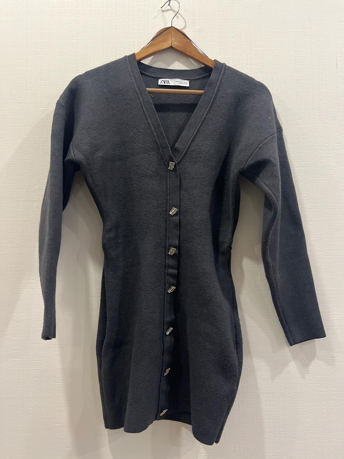 Dark gray cardigan or knit dress with silver buttons and a V-neck, hanging on a wooden hanger. ZARA label visible on the collar.