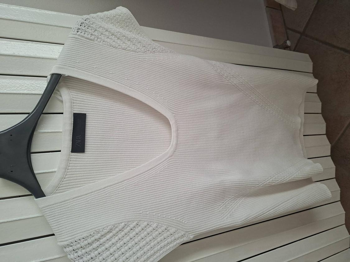 White ribbed knit T-shirt with short sleeves and openwork detail on the shoulders, hanging on a black hanger.