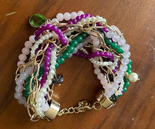 Multicoloured beaded bracelet with gold chains on a wooden surface. Includes green, purple, white, and pink beads.