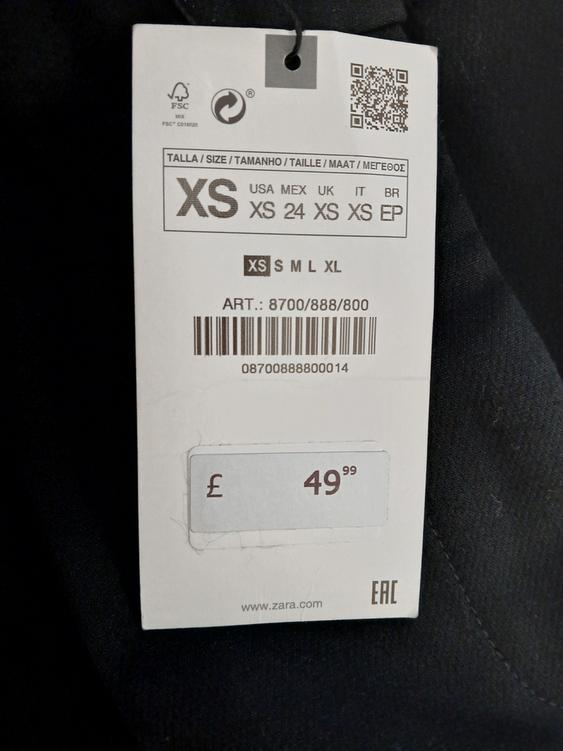 Clothing label on black fabric, showing size XS and price £49.99. Includes barcode and website www.zara.com.