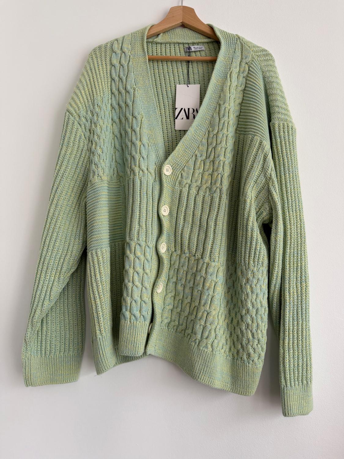 Light green, chunky knit cardigan with white buttons, hanging on a wooden coat hanger. Label visible with the text "ZARA".