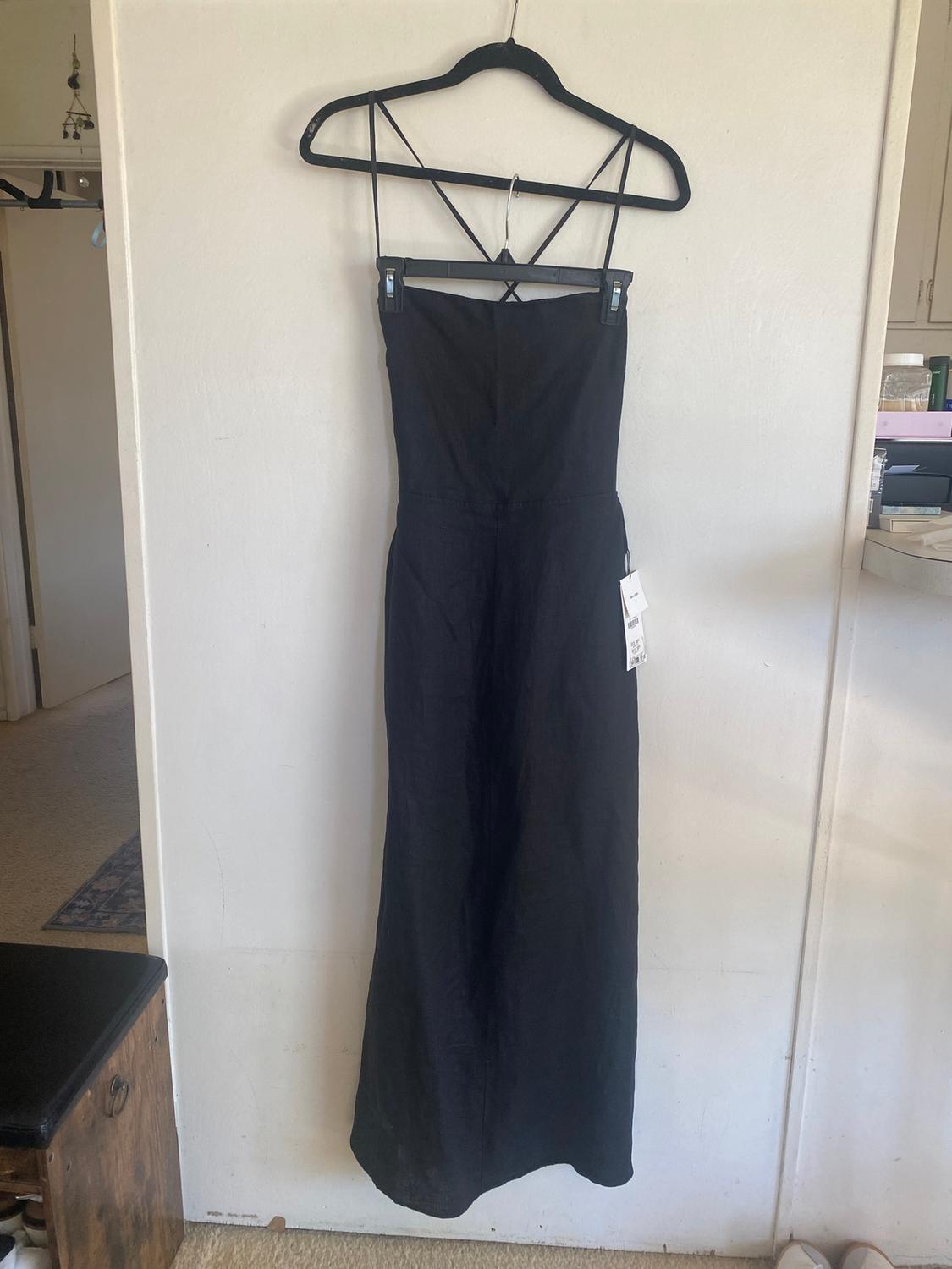 Long black dress with thin criss-cross straps on the back, hanging on a black hanger against a white wall.