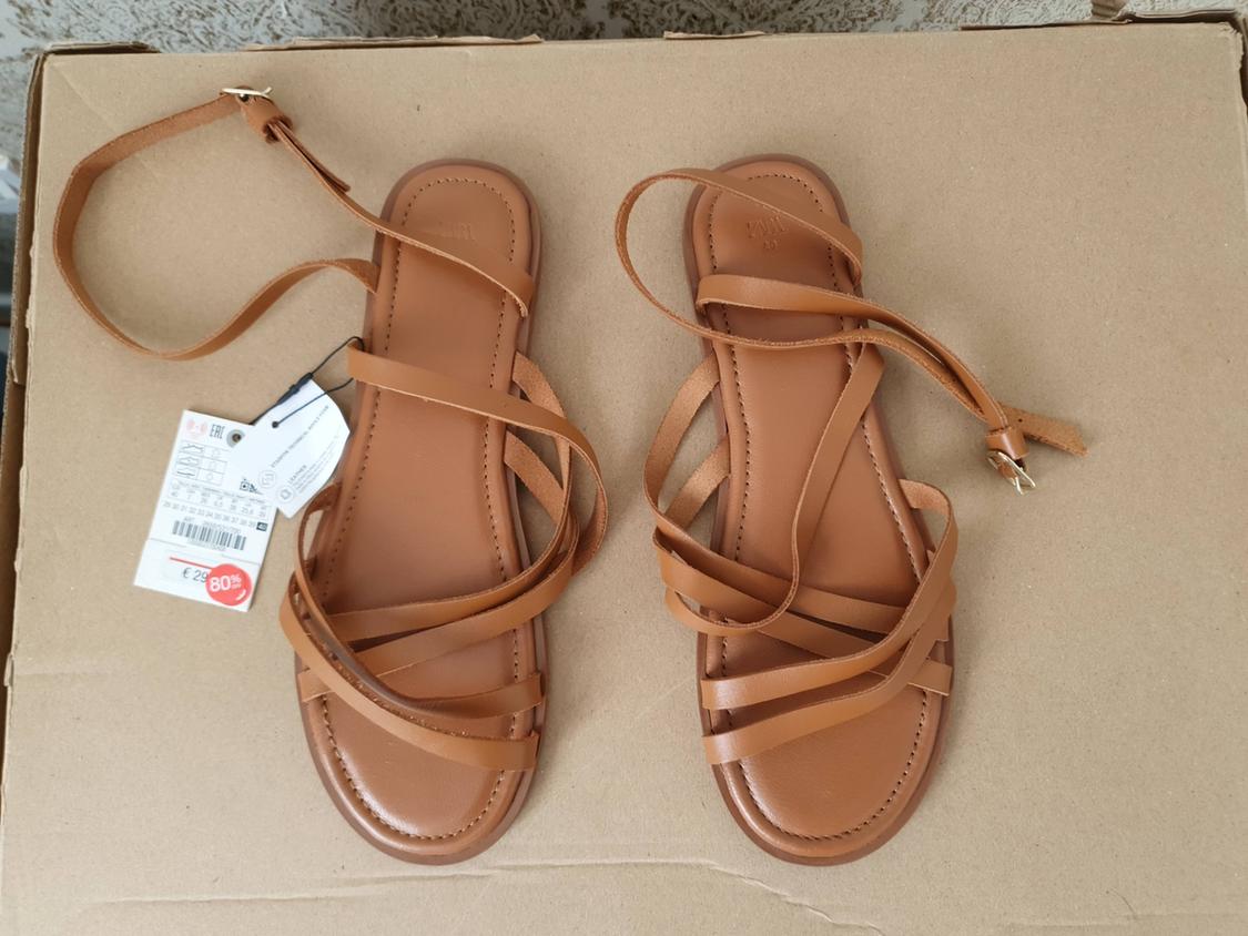 Brown strappy sandals on a cardboard box, with a price tag showing an 80% discount.
