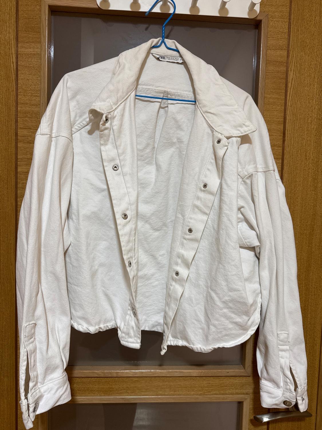 White jacket hanging on a blue hanger over a wooden door. The jacket has buttons and a wide collar.