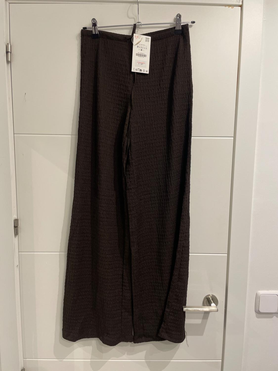 Textured black trousers hanging on a white door. Visible label with product details.