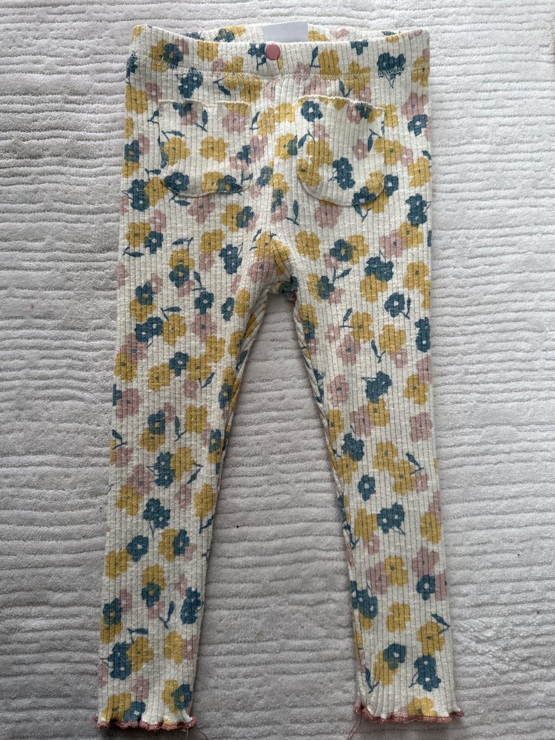 Front view of trousers with floral print in yellow, blue and pink shades, with back pockets.