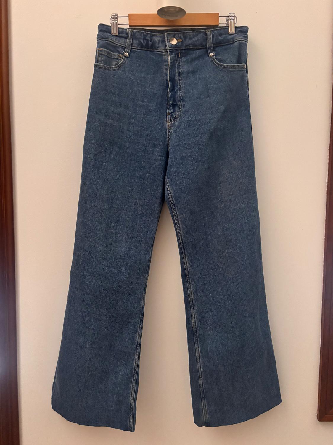 Blue wide-leg jeans hanging on a wooden hanger against a light background.