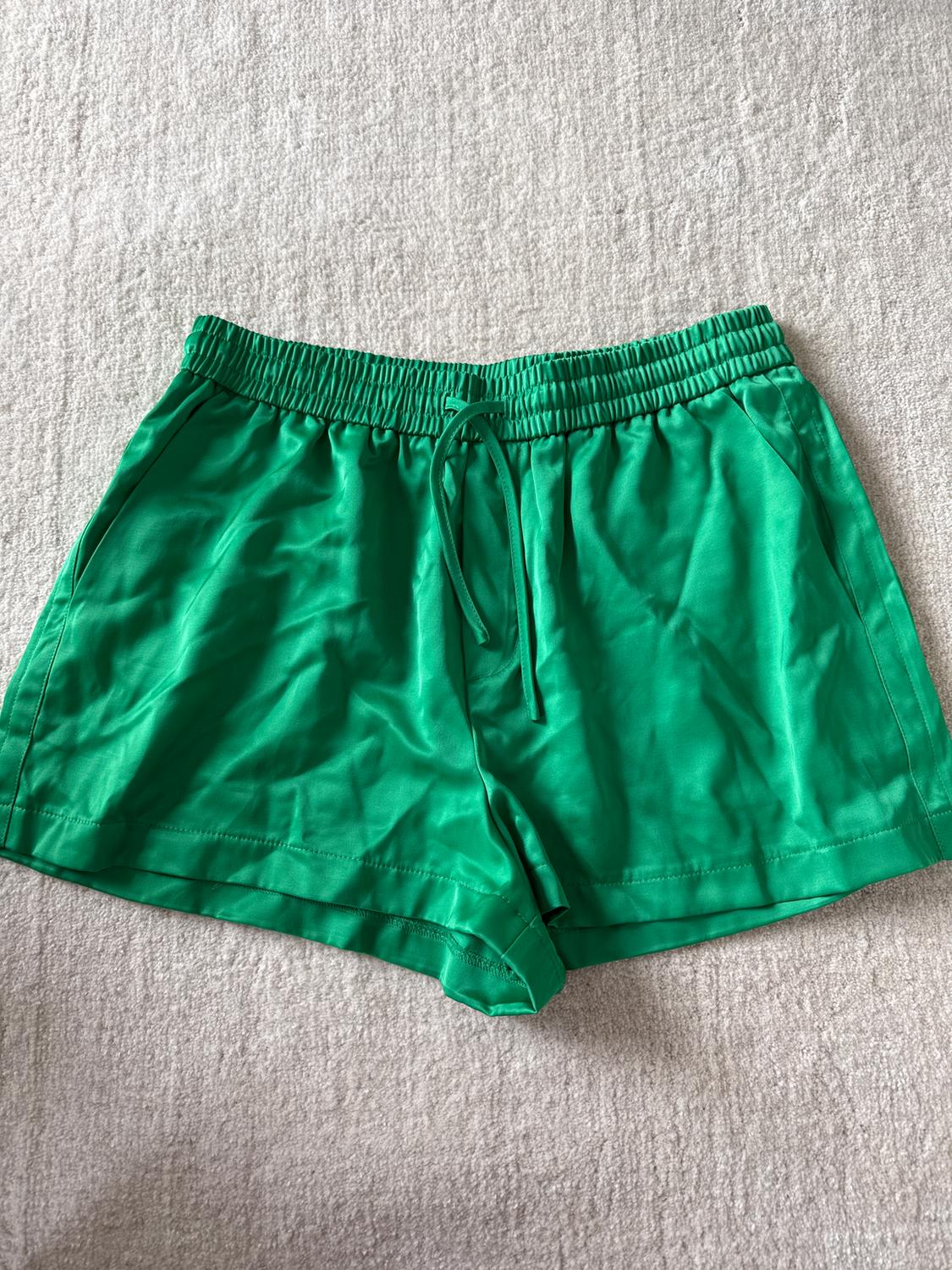 Green shorts with an elasticated drawstring waist, on a textured beige surface.