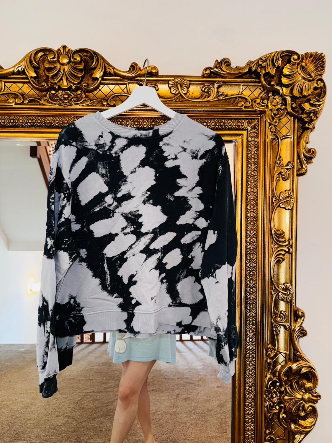 Abstract black and white design sweatshirt hanging in an ornate gold frame. Interior background with carpet and white wall.