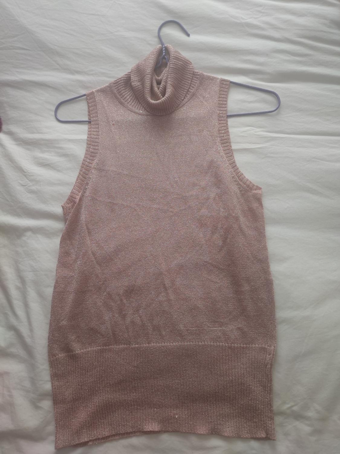 Pink high-neck sleeveless jumper, hanging on a hanger against a white surface.