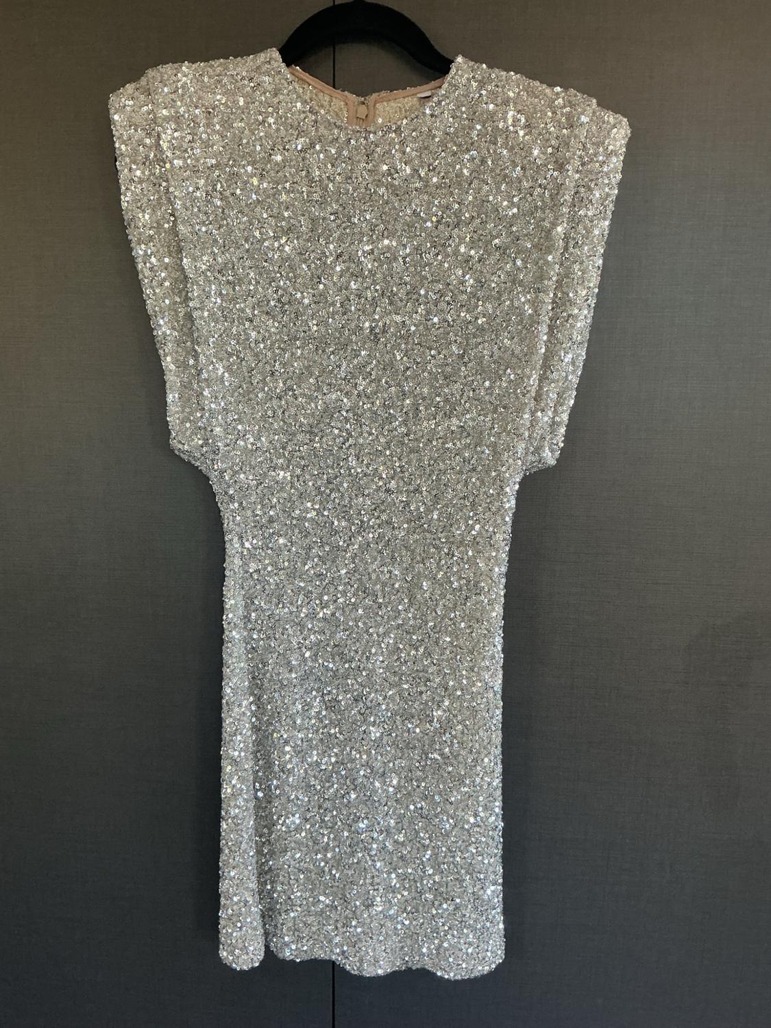 Sparkling silver sequin dress hanging on a black hanger against a dark wall.