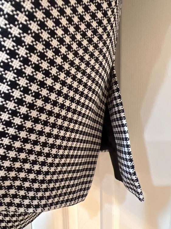 Close-up of a garment with a black and white houndstooth print, showing a side slit detail.