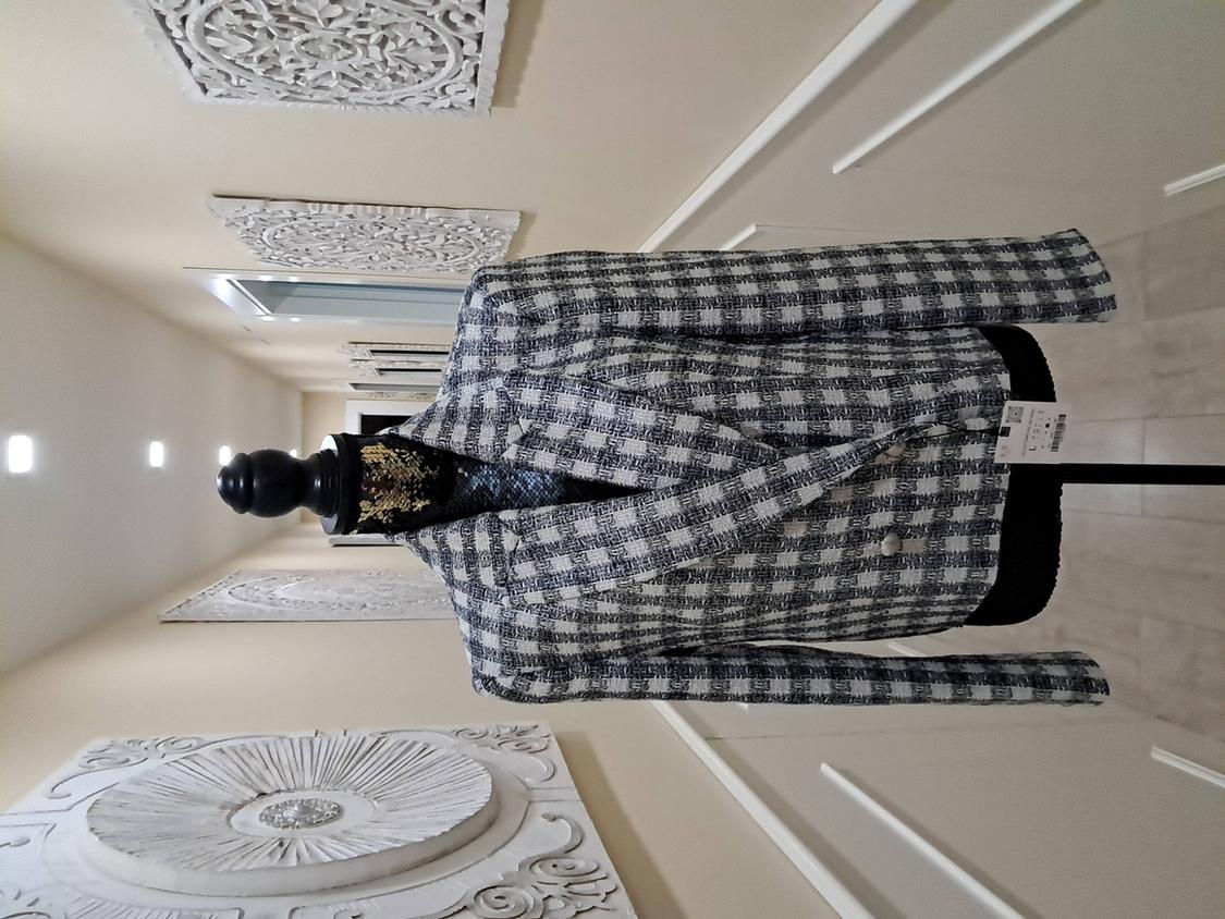 Mannequin in a black and white checked jacket, in a hallway with carved relief wall decorations.