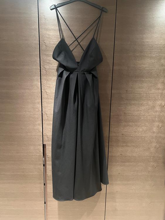 Black dress hanging on a hanger, with criss-cross straps and a V-neck, against a light wooden background.