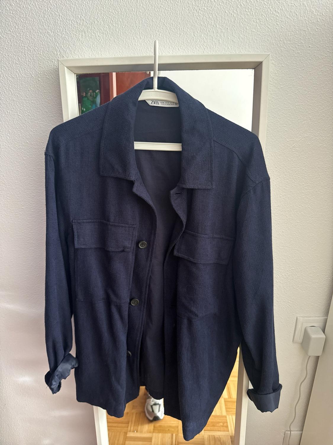 Σkura μπλε σκούρα μαρυκομάνικα overshirt με μπροστινές τσέπες, κρεμασμένη σε κρεμάστρα μπροστά από καθρέφτη. Ετικέτα με το κείμενο ZARA.