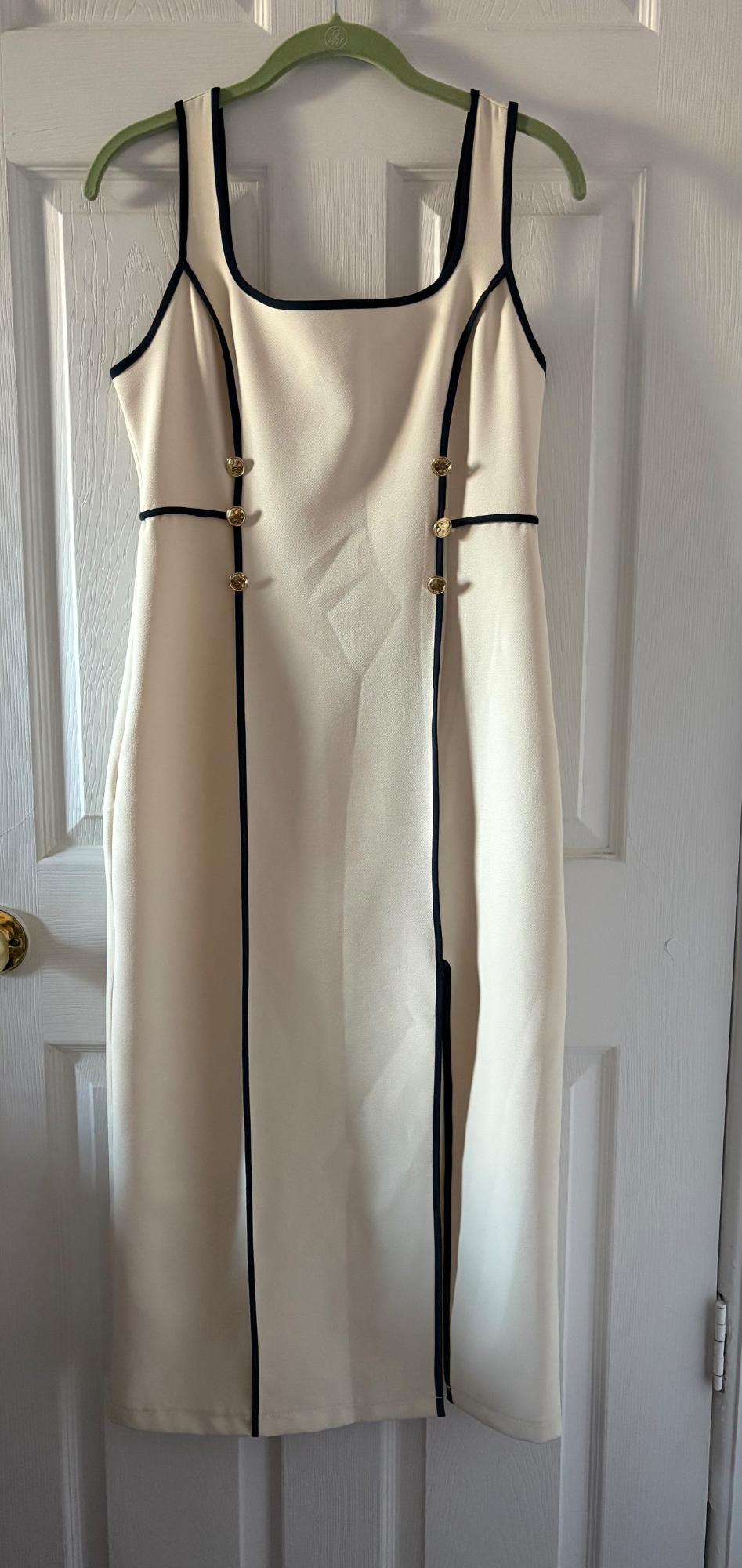 White sleeveless dress with black trim and gold buttons, hanging on a green hanger over a white door.