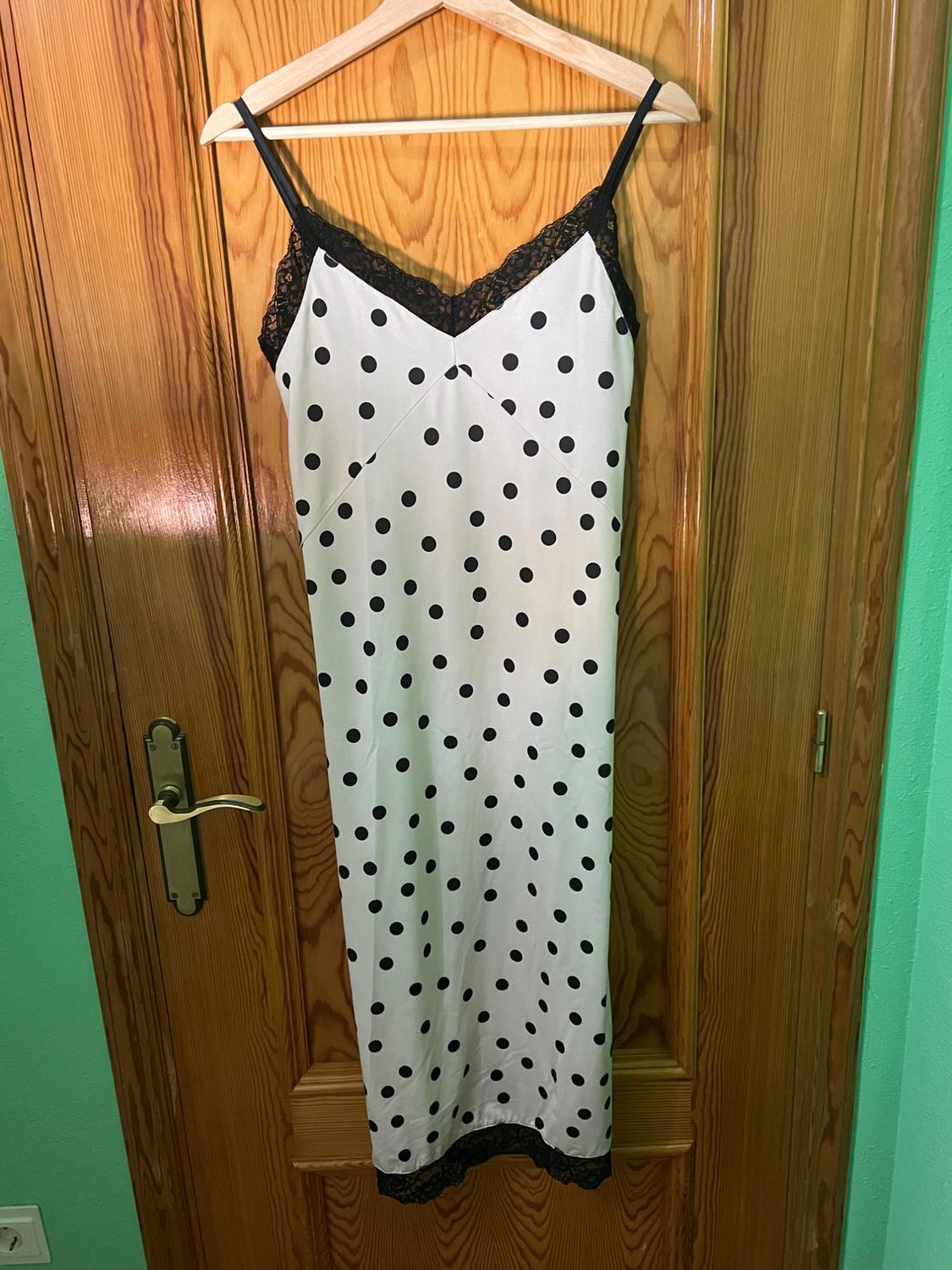 White dress with straps and black polka dots, lace details on the neckline and hem, hanging on a wooden door.