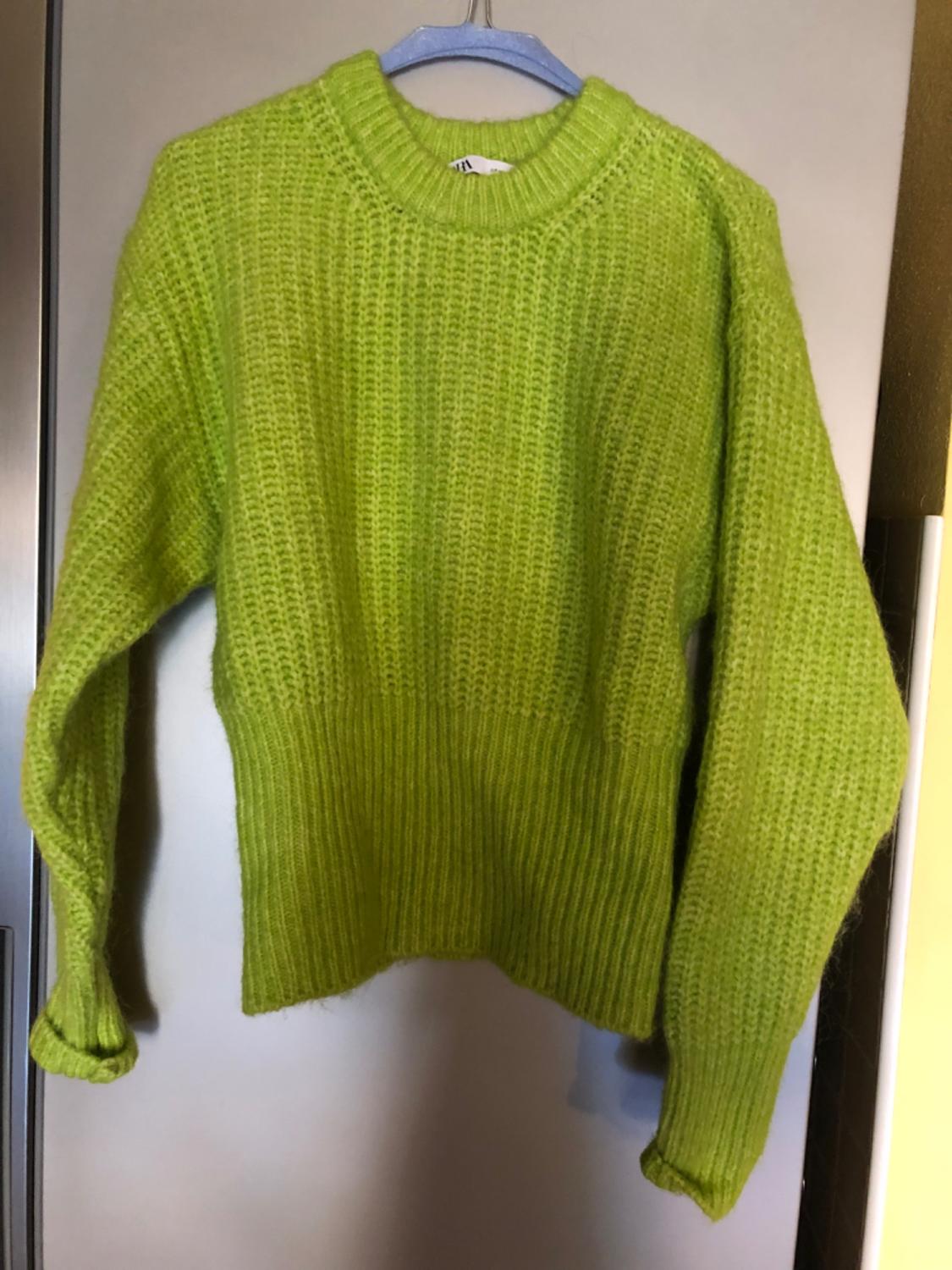Lime green chunky knit jumper hanging on a blue hanger, against a neutral backdrop.