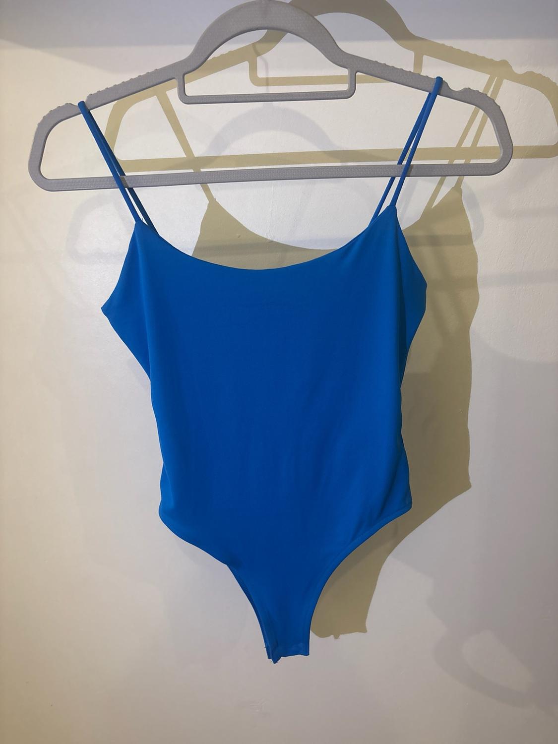 Blue bodysuit with thin straps hanging on a grey hanger against a white background with a drop shadow.