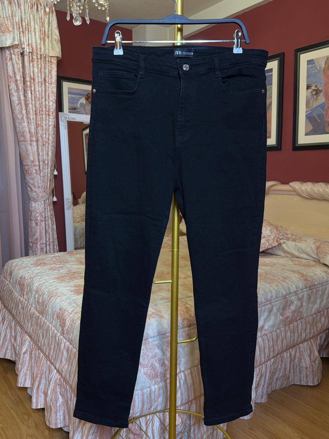 Black trousers hanging on a gold hanger in a bedroom with red walls and a bed with a patterned bedspread.