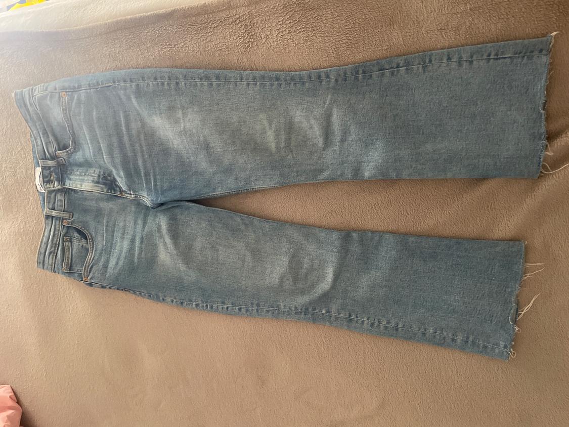 Light blue jeans with a frayed hem, laid out on a textured beige blanket.